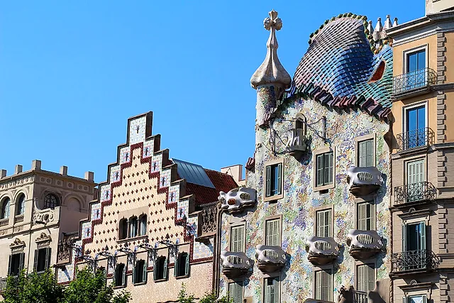 The stepped gable of Casa Amatller beside the tiled roof, turret and cross of Casa Batlló, seen from the street