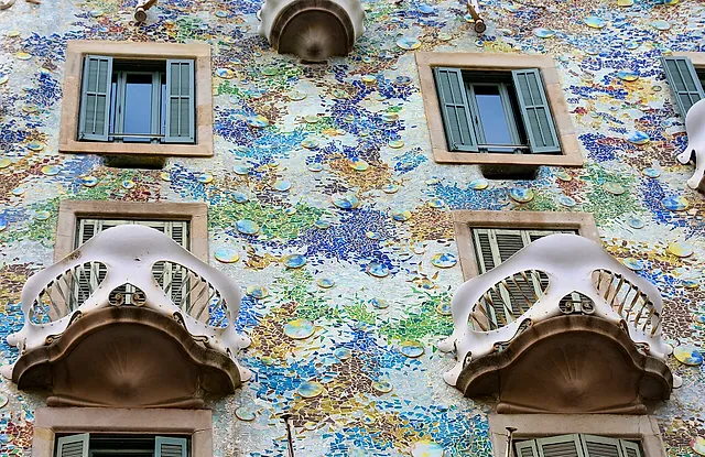 Two of the bone-like balconies of Casa Batlló against the facade covered in blue, green and ochre mosaic fragments