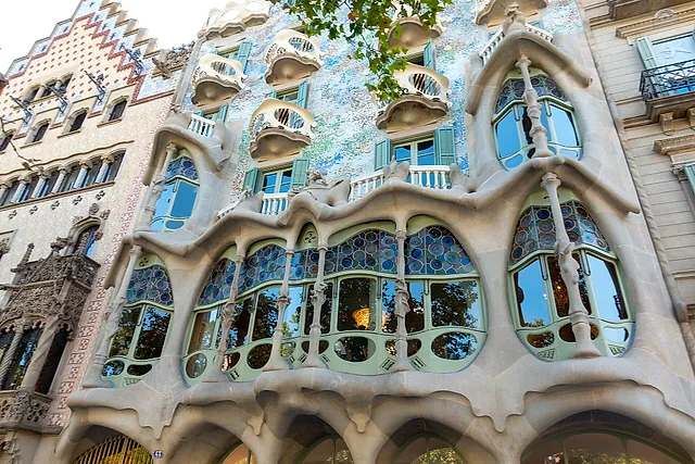 The main facade of Casa Batlló on Passeig de Gràcia in daylight, with its wavy stone balconies, blue-green mosaic wall and tiled roof