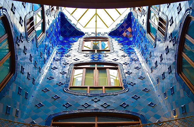 The central light well of Casa Batlló, its walls covered in tiles that shade from deep blue at the top to paler blue below, with the skylight above