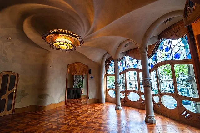 The main salon of the noble floor of Casa Batlló with its swirling plaster ceiling, wooden floor and stained-glass windows onto the street